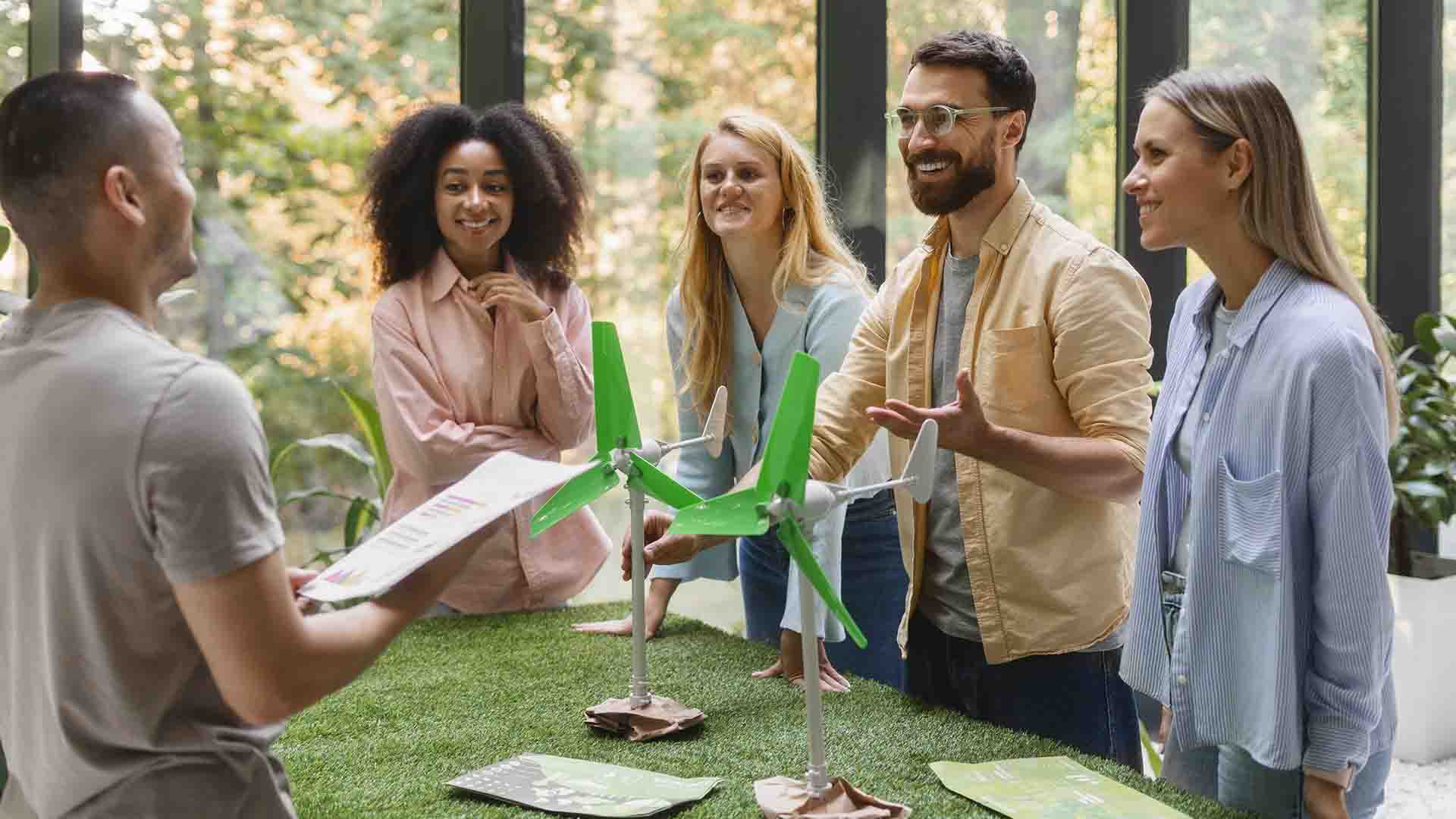 Equipo analizando miniatura de turbina eólica, representando regalos ecológicos creativos e innovación sostenible en las empresas.